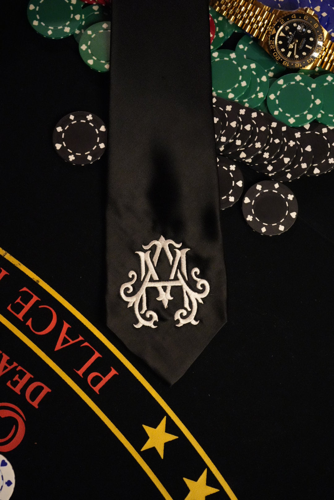Poker chips, a watch, and a card with a decorative logo on a black background